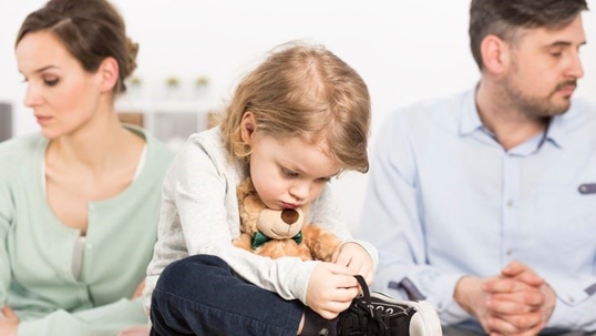 A sad child with parents in the background looking away in the opposite direction.